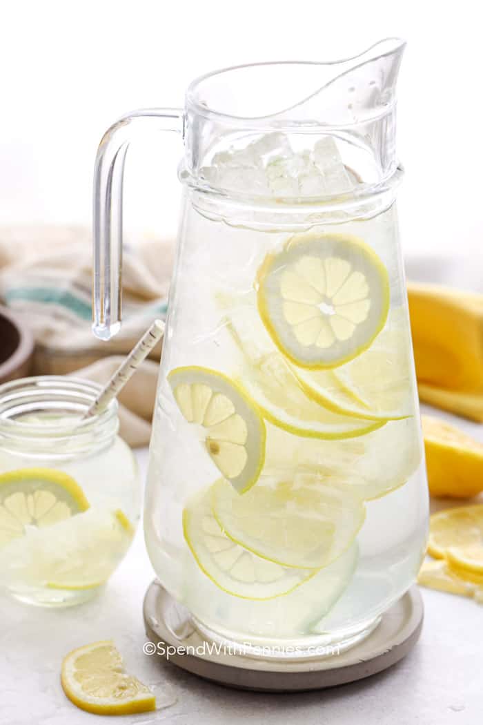 Big glass jar of Lemon Water with small glass next to it