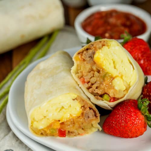 Breakfast burrito on a plate cut in half with strawberries on the side