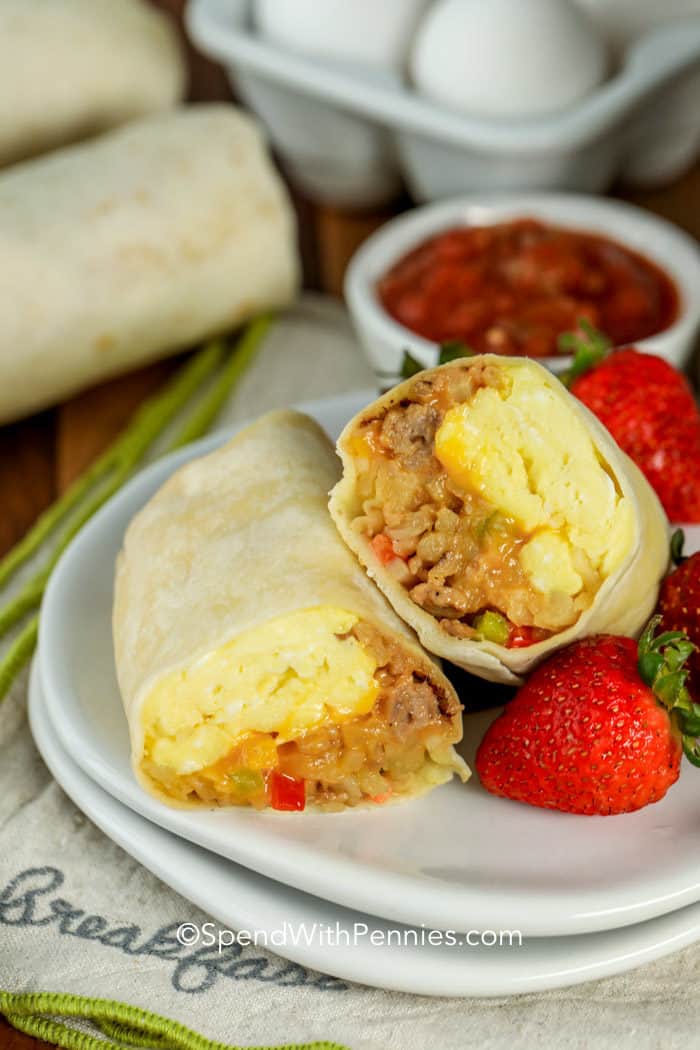 Breakfast burrito on a plate cut in half with strawberries on the side