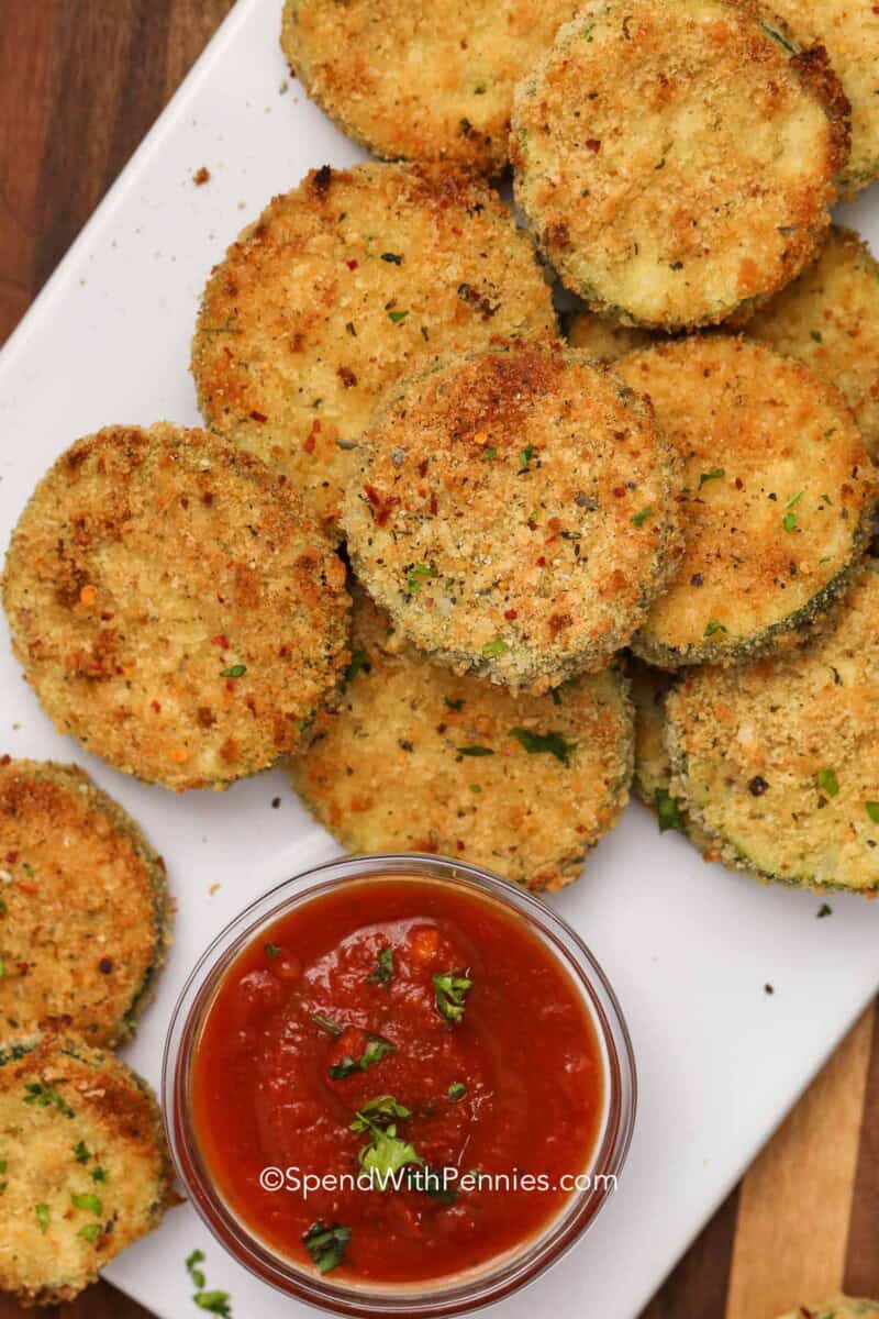 Make fried zucchini medallions with simple ingredients like zucchini, eggs, flour, parmesan cheese, and seasoned breadcrumbs. Each slice cooks quickly in hot oil, giving you a crisp coating and tender center without a long prep time. This recipe is perfect for summer zucchini, family dinners, game day snacks, or a warm appetizer served with your favorite dip. Pin this zucchini recipe for your next pasta night. #spendwithpennies fried zucchini on a plate with marinara sauce