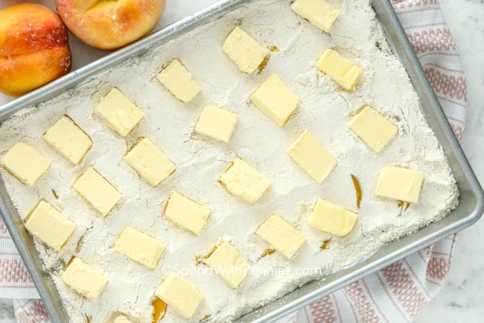 Overhead shot of pads of butter on top of peaches in a baking dish