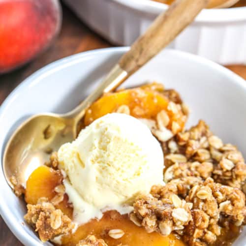 Peach Crisp in a white bowl with a spoon and vanilla ice cream