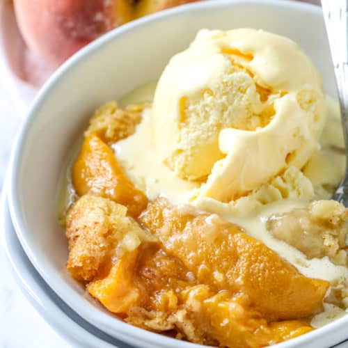 Peach Dump Cake in a white bowl with vanilla ice cream