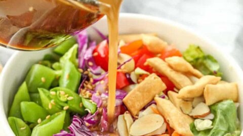 Sesame Ginger Dressing being poured over a salad in a bowl.