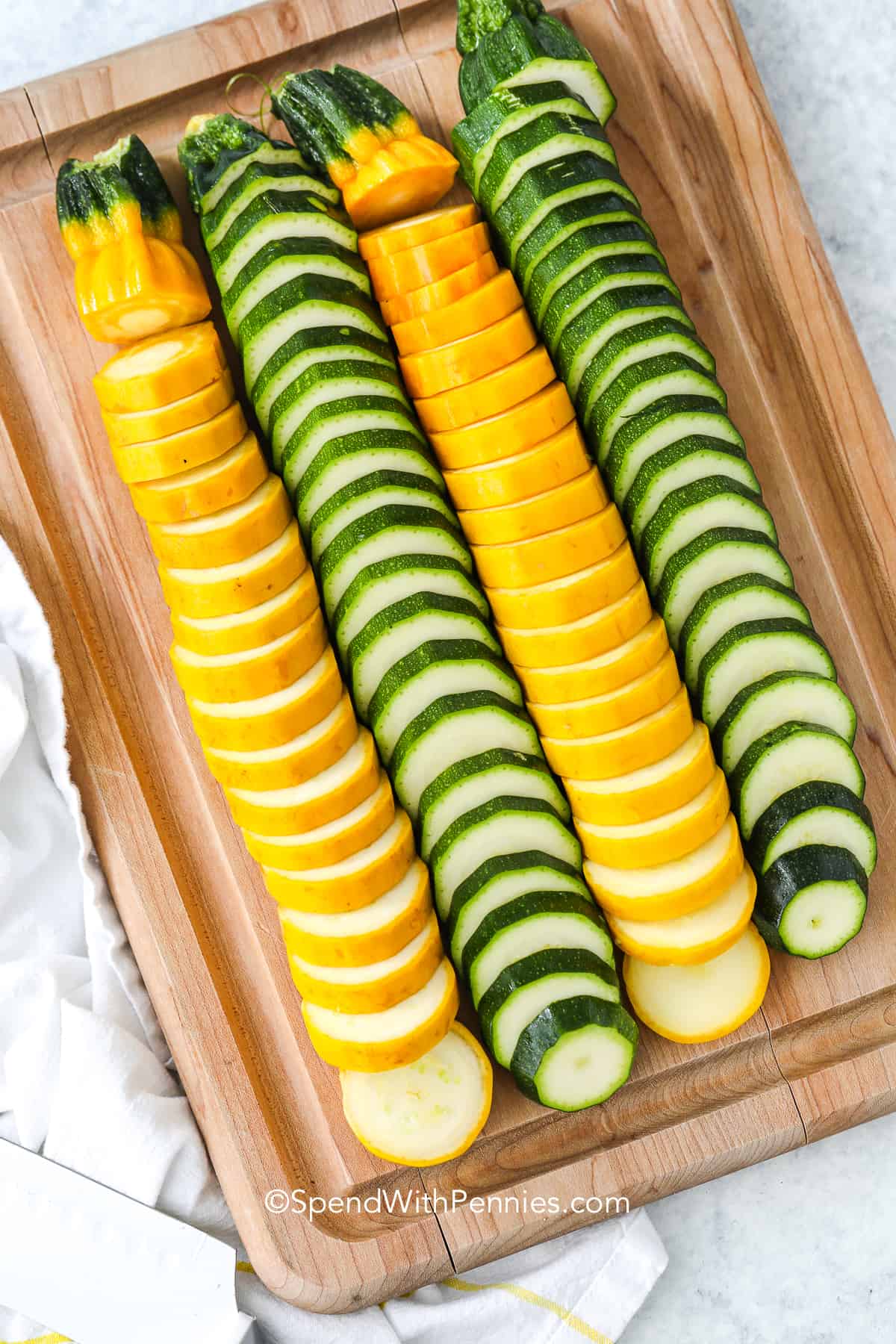 slice yellow summer squash and zucchini on a wood cutting board