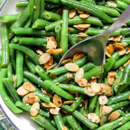 Green bean almondine in a dish with a metal Serving Spoon