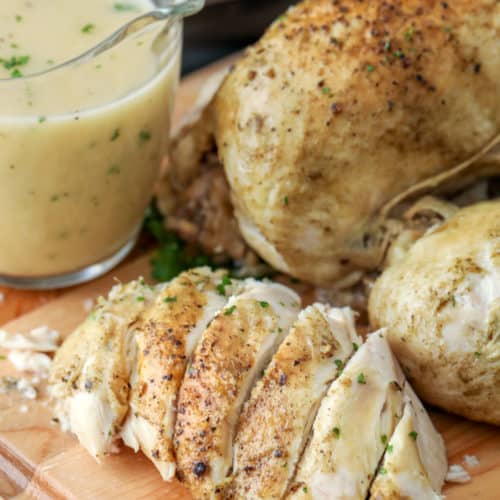 Instant pot whole chicken on a wooden board cut into slices with gravy on the side