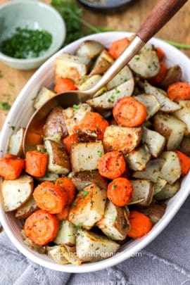 Roasted potatoes and carrots in a white dish with a spoon