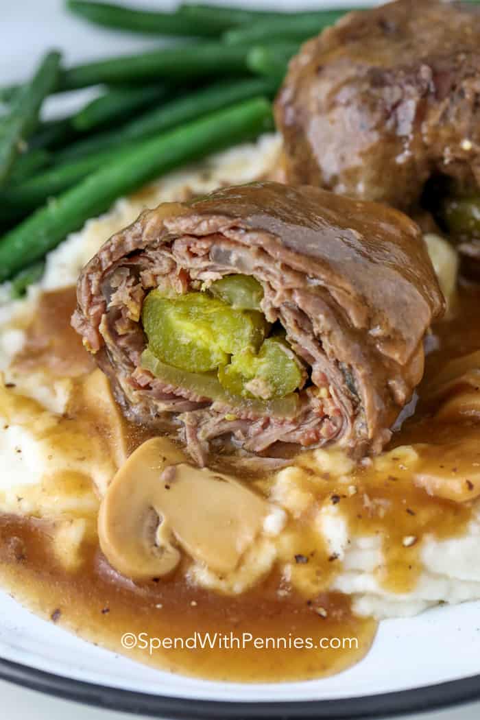 Beef rouladen on mashed potatoes with gravy and green beans in the background