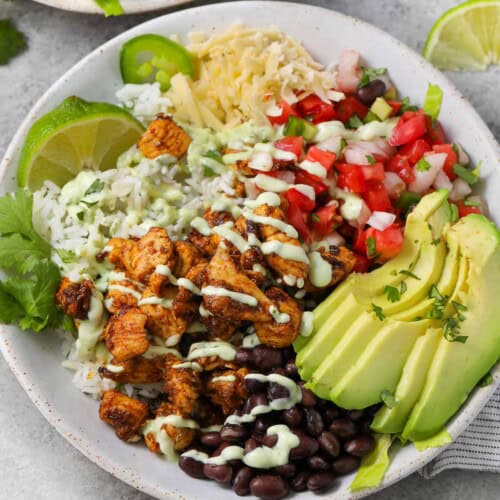 A chicken burrito bowl with avocado and pico de gallo and lime