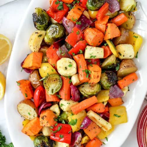 Roasted vegetables with smashed garlic on a white serving plate