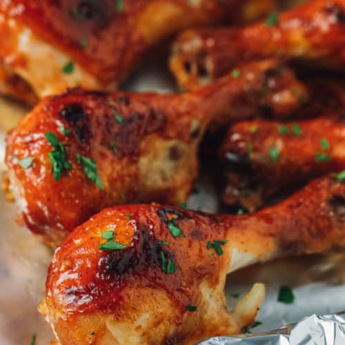 Sticky chicken drumsticks on tin foil garnished with parsley