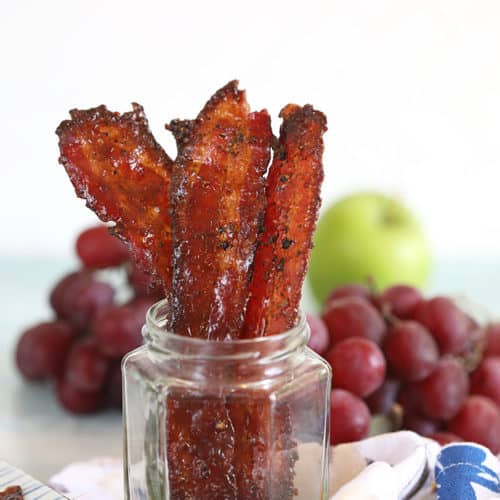 Candied bacon in a clear jar with grapes in the background