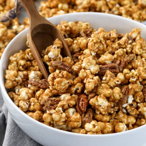Caramel corn in a white bowl with a wooden scoop