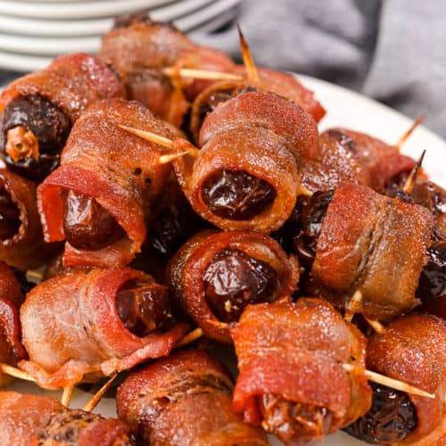 Bacon wrapped dates on a marble board with plates in the background