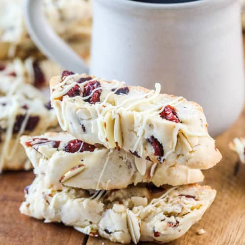 stack of almond biscotti on a wooden board with a cup of coffee in the background