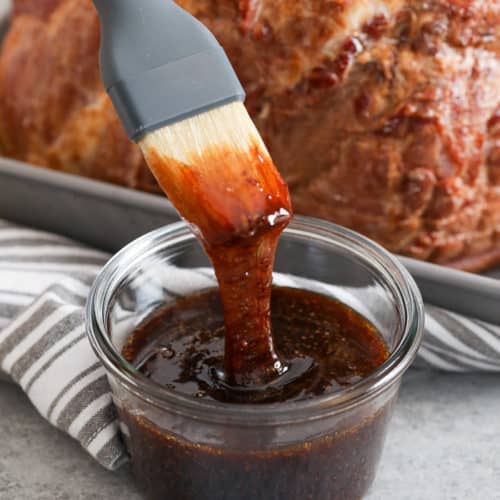 Brown sugar glaze in a jar with a brush and a ham in the background