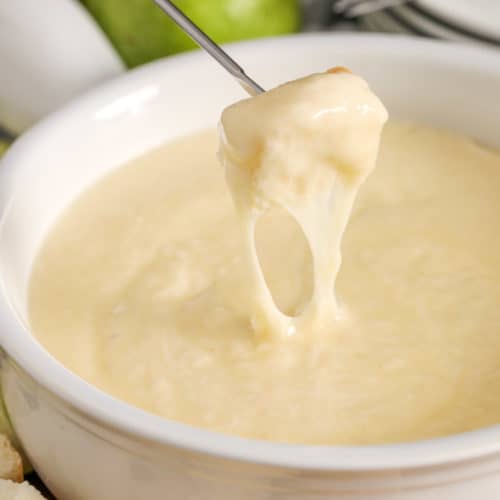 Cheese fondue in a white Bowl being dipped with bread from a fondue skewer