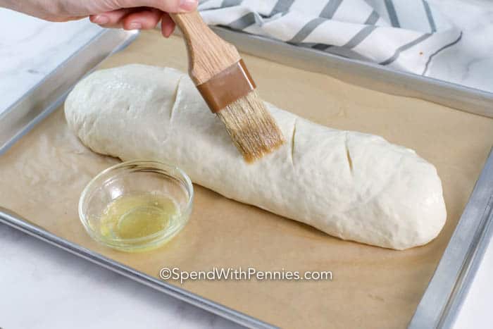 French bread loaf being brushed with melted butter mixture before baking.