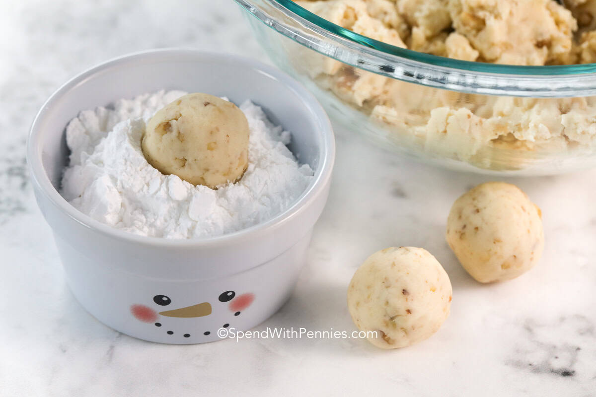 dipping snowball cookie dough in a bowl of powdered sugar