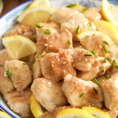 Lemon chicken lemon chicken in a bowl with sesame seeds chives and lemons