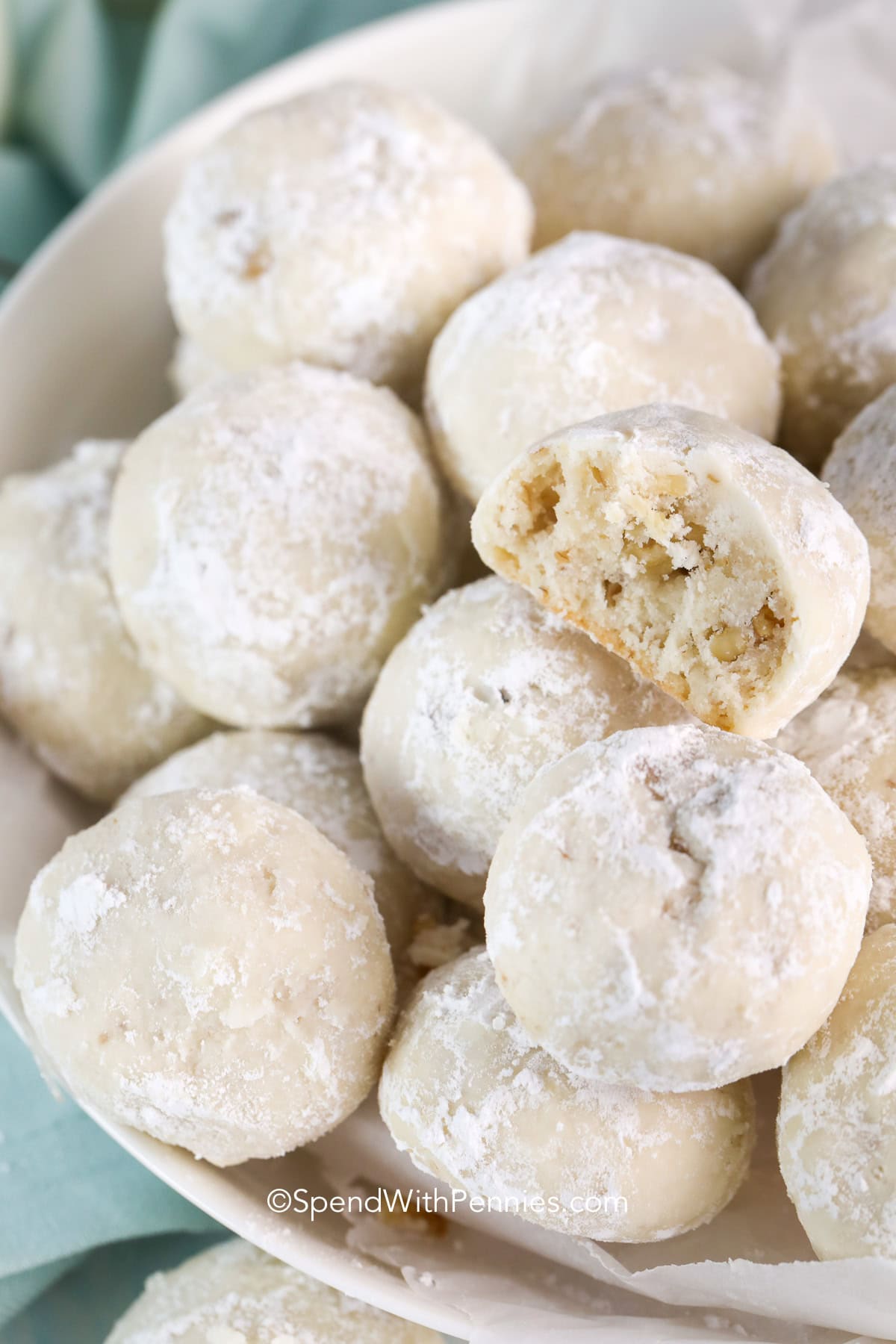Snowball cookies in a bowl with a bite out of one cookie