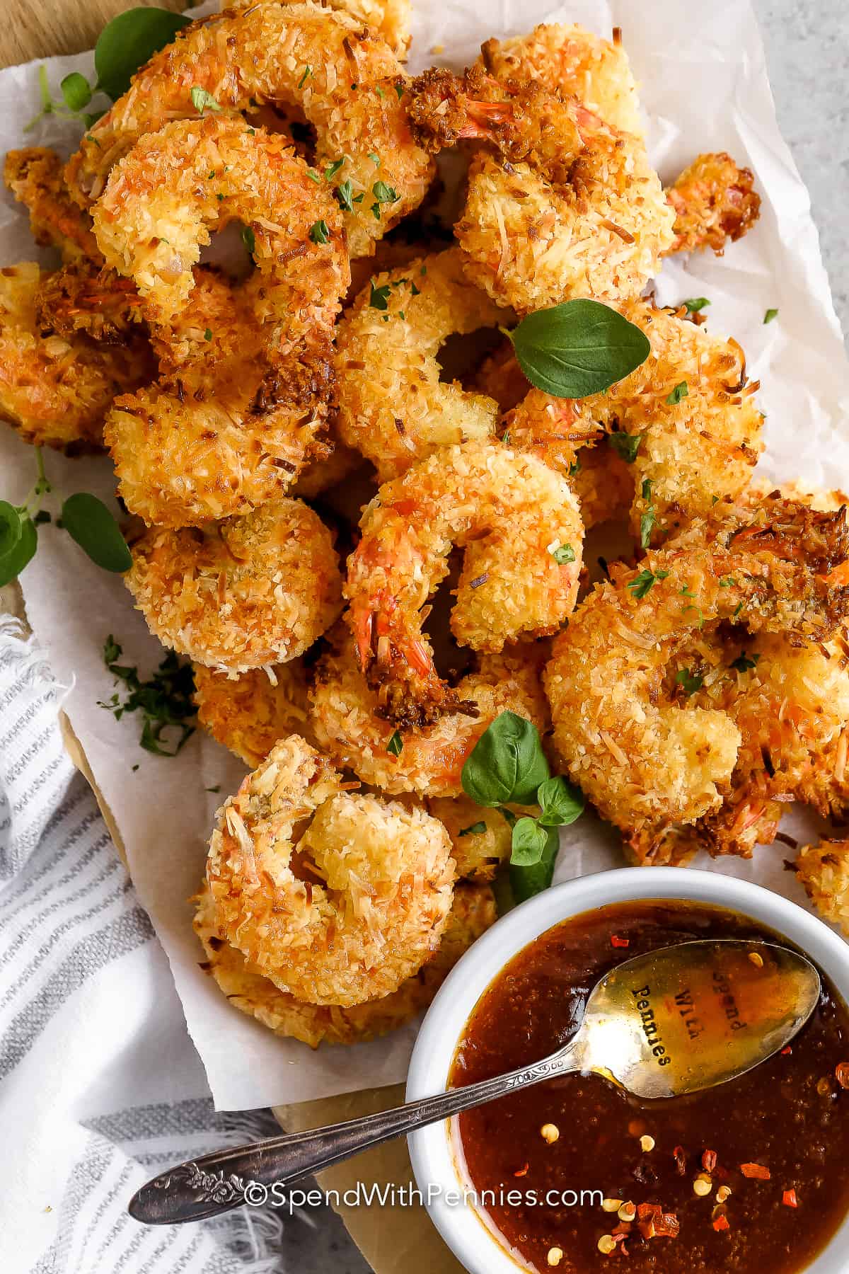 Coconut Shrimp is super sweet and super juicy! Jumbo shrimp tossed in coconut & flour and baked until golden crispy, these tasty little morsels are perfect for a party, a potluck, or as an appetizer. #coconutshrimp #coconutshrimprecipe #easycoconutshrimp #spendwithpennies a plate of coconut shrimp with sweet chili sauce