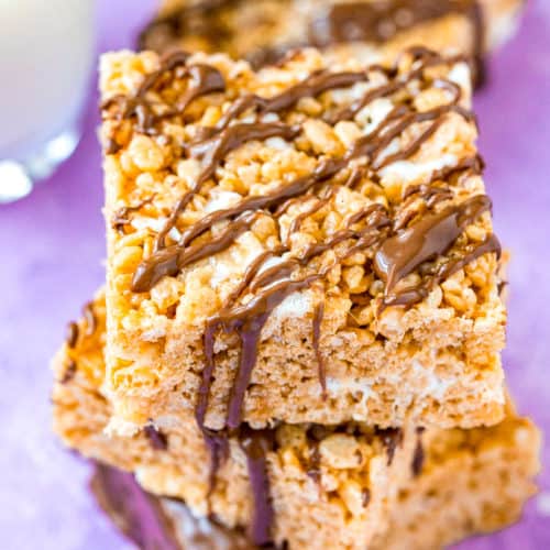 Three rice krispies treats drizzled with chocolate stacked on top of each other.