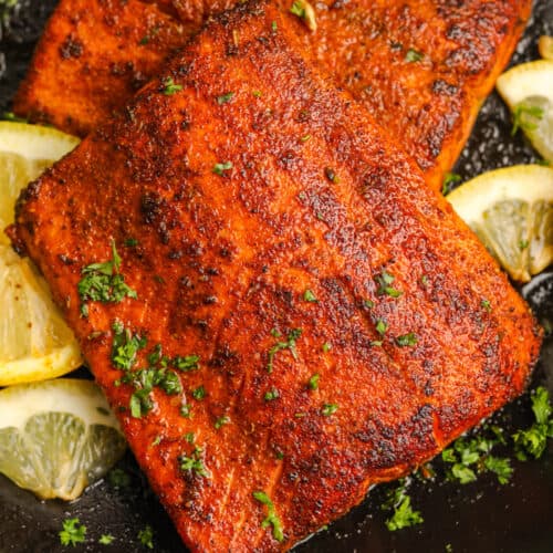 two pieces of cooked blackened salmon topped with parsley and served with lemons