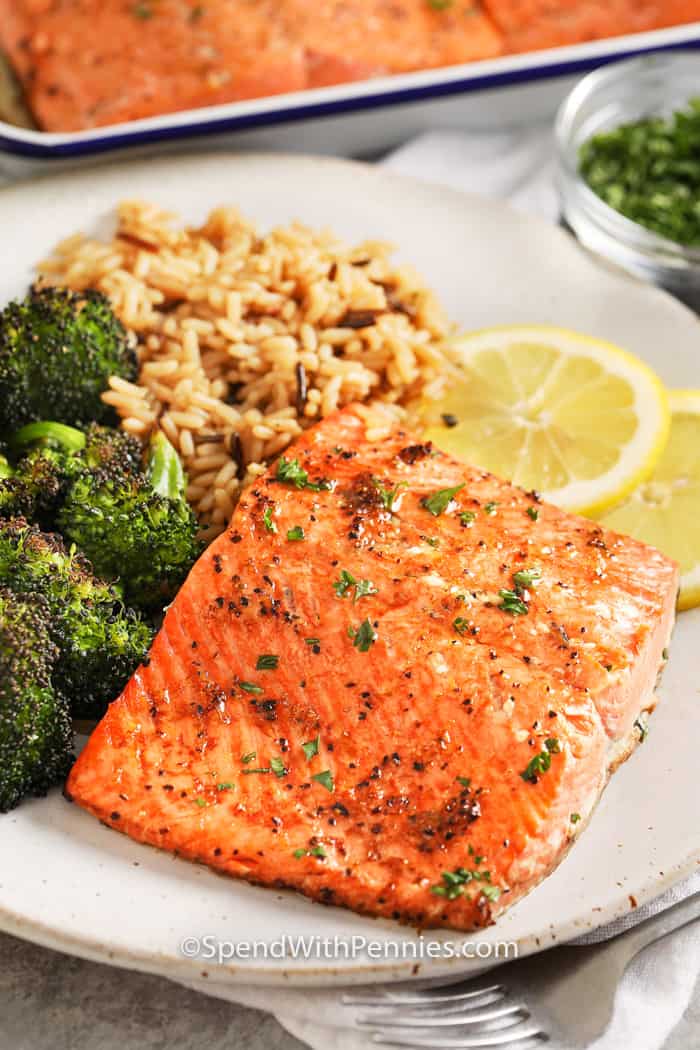 A broiled salmon filet served with broccolie and rice, with two lemon slices on the side. 