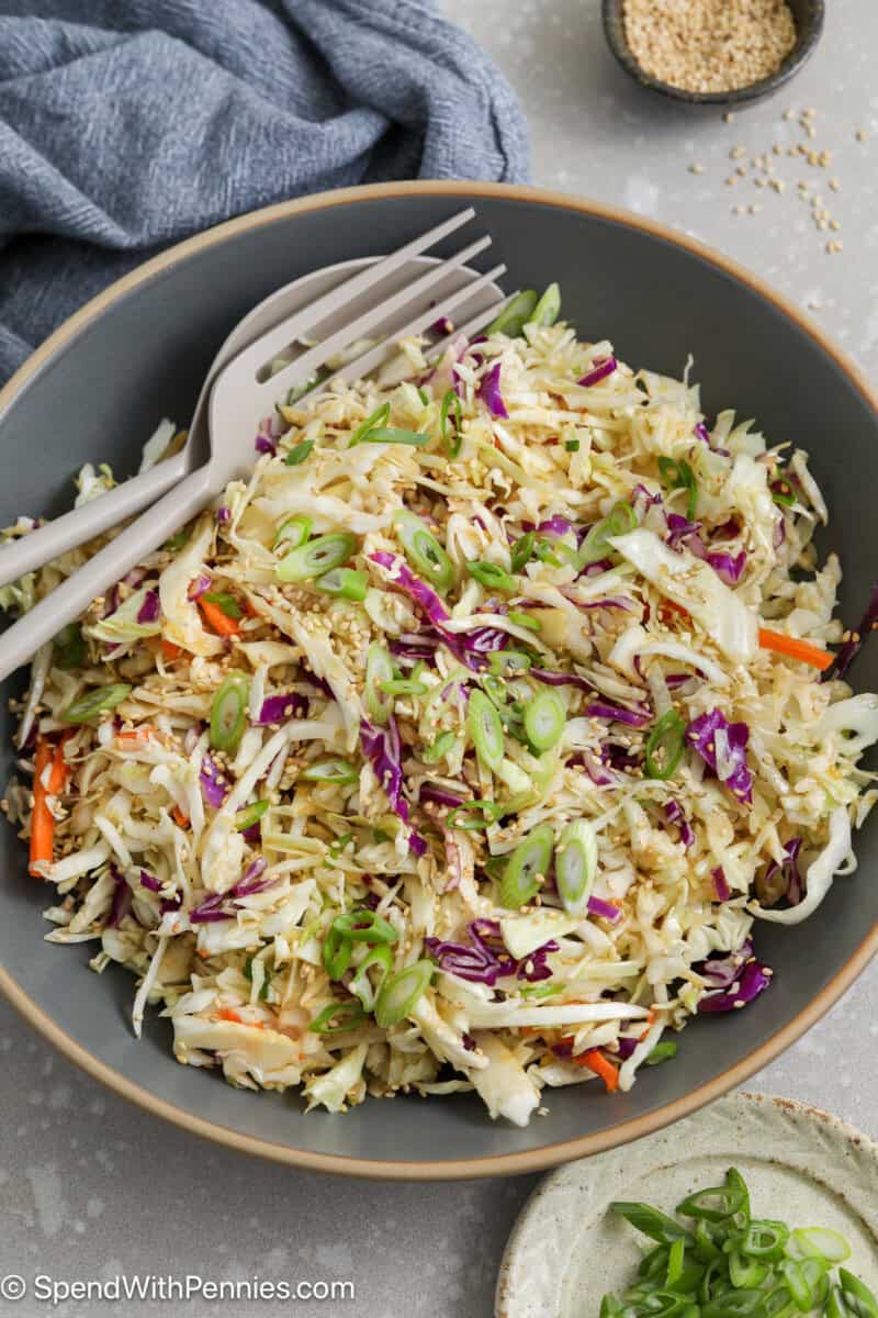 Asian slaw in a serving bowl with utensils