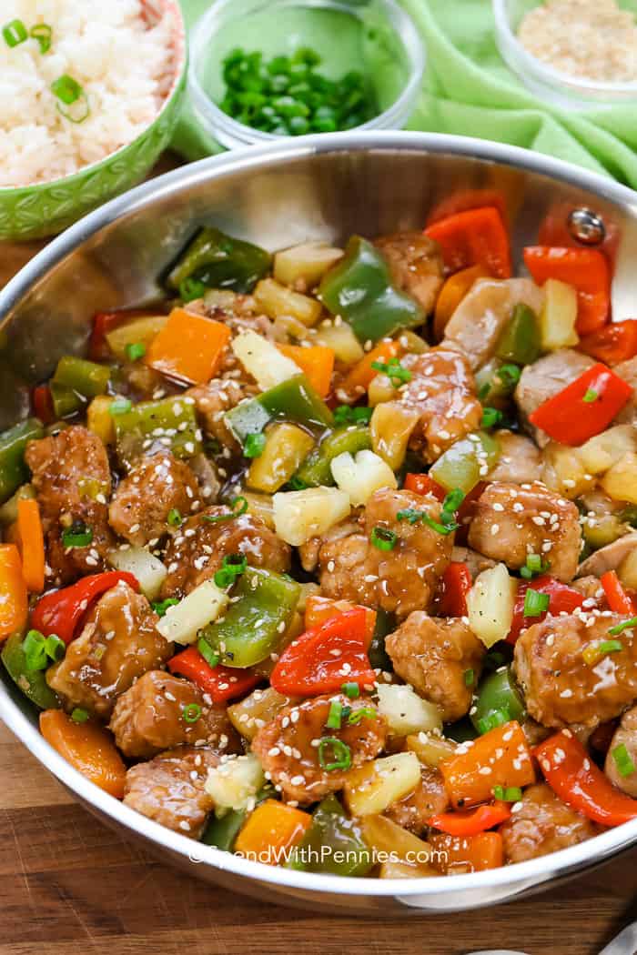 Sweet and sour pork in a pan with sesame seeds and green onions