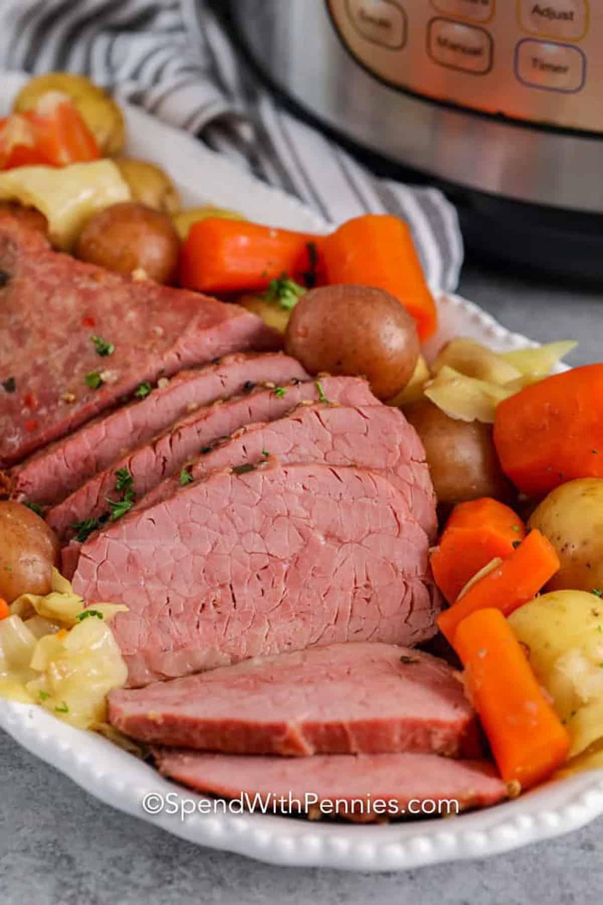 Instant Pot Corned Beef is a simple recipe to prepare. Made with potatoes, carrots, and cabbage this easy recipe is perfect for St. Patricks Day or any day of the year! #instantpotcornedbeef #cornedbeefbrisket #instantpot #spendwithpennies corned beef on a plate with vegetables and an instant pot in the background