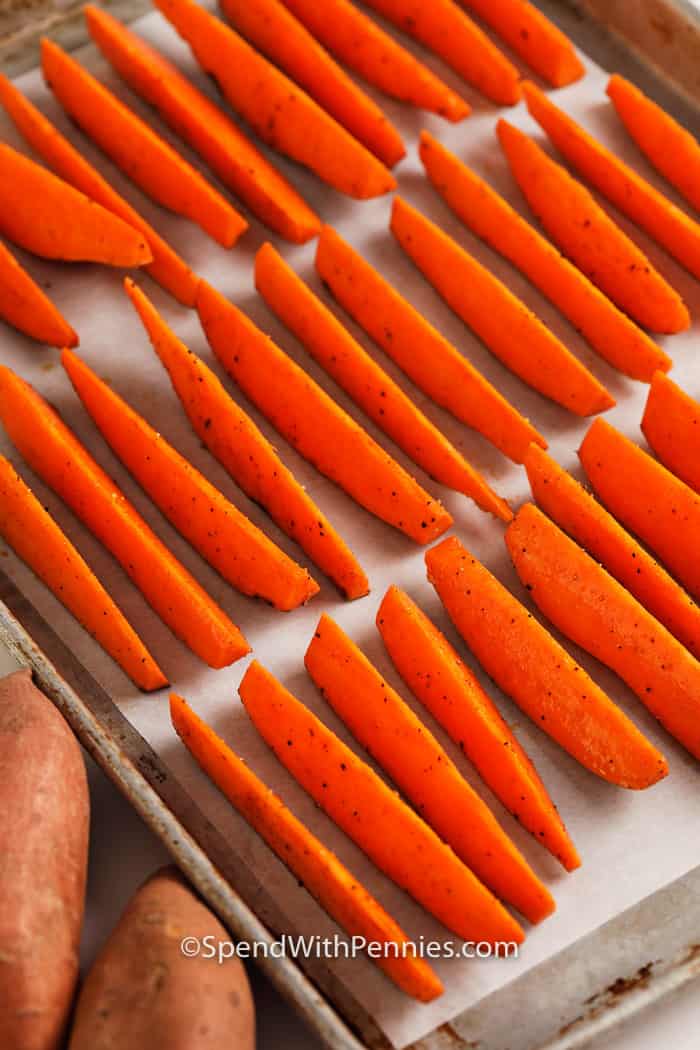 We love making these homemade baked sweet potato fries at home for an easy and delicious addition to any meal! They pair perfectly with any entree including fried chicken, burgers, or even enjoy them on their own as a tasty snack. #sweetpotatofries #fries #yamfries #spendwithpennies Sweet potato fries lined up on a baking sheet