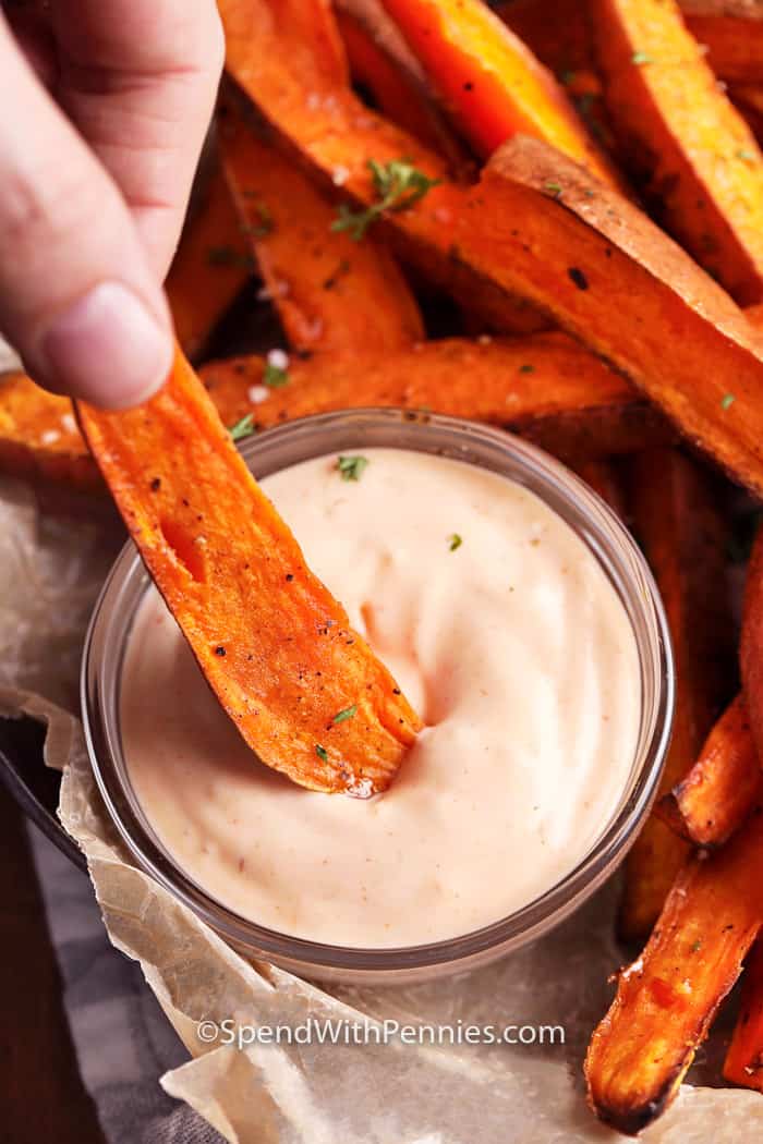 Sweet Potato Fries are baked in the oven for maximum flavor & crispiness, without the added fat of traditional deep-frying. We love serving these fries with aioli or mayo as a side dish for burgers, chicken, or even steak! #sweetpotatofries #fries #yamfries #spendwithpennies Sweet potato fries being dipped in aioli