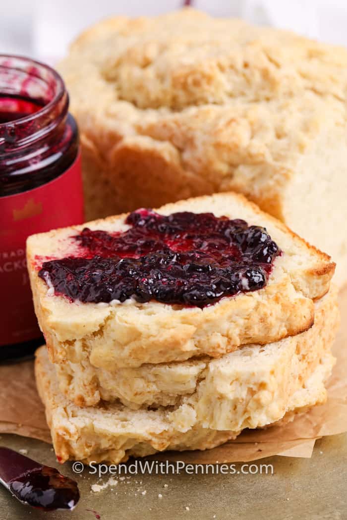 This baked beer bread recipe is super easy to make with super simple ingredients. With no rise time and no yeast, this bread comes together quickly. Serve for breakfast with jam or with soup or chili! #beerbread #easybreadrecipe #homemadebeerbread #spendwithpennies Sliced beer bread topped with jam