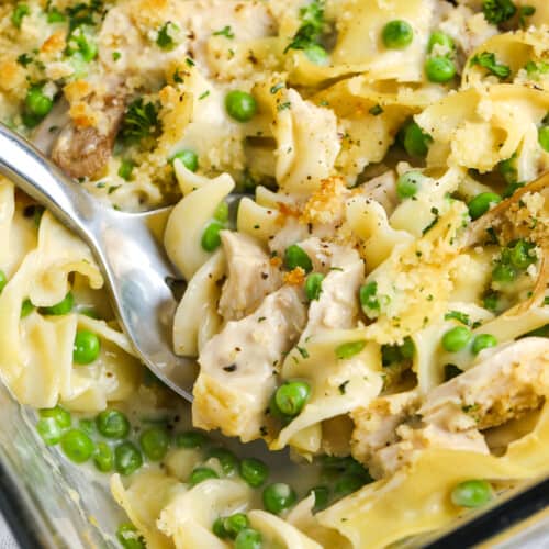 Serving chicken noodle casserole from a baking dish with a silver serving spoon
