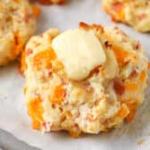 butter on top of baked ham and cheese drop biscuits on a baking pan