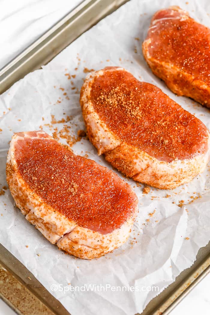 Oven-baked pork chops are a foolproof recipe that’s both simple and satisfying, making it a go-to for busy weeknights! These pork chops are seasoned with a flavorful brine and a quick rub before being baked and finished with a broil for extra caramelization. The result? Juicy, tender pork chops that are bursting with delicious flavor in every bite. #spendwithpennies Seasoned pork chops on a baking tray