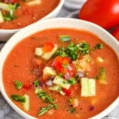 Gazpacho in a bowl with tomatoes behind