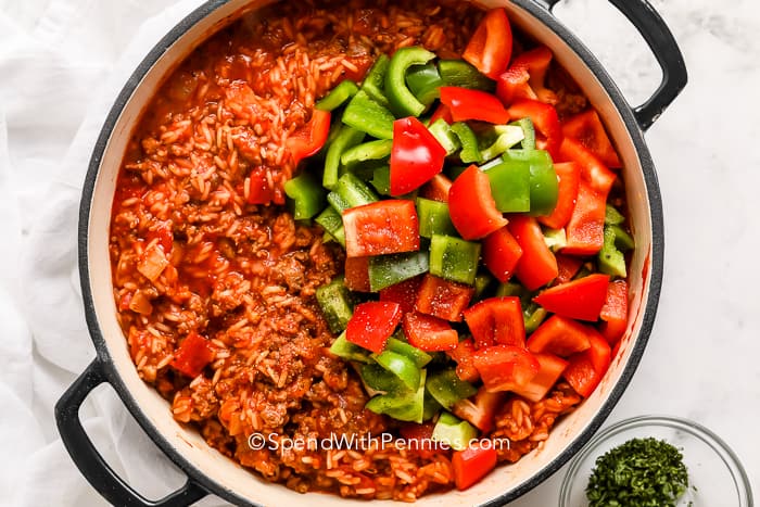 green and red bell peppers on top of sausage cooked with rice in tomato sauce