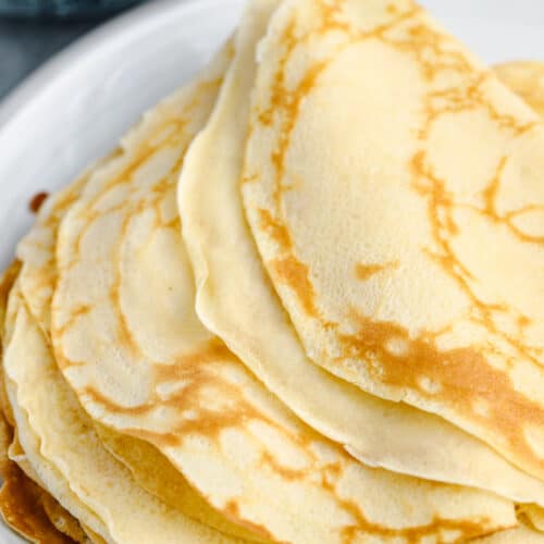 pile of crepes on a plate with a bowl of blueberries to make Blueberry Crepes