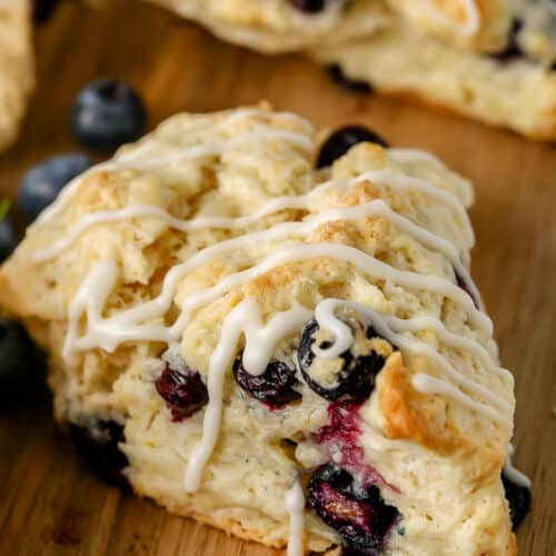 a blueberry scone with drizzle on a wood cutting board