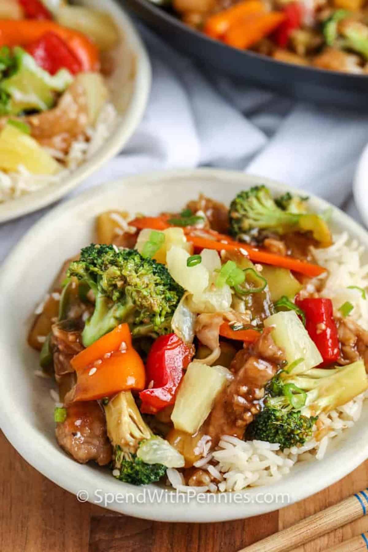 This pork stir fry is a saucy, colorful dinner that is easy enough for a weeknight. Tender pork strips, mixed vegetables, garlic, ginger, and pineapple are cooked in a large skillet, then coated in a homemade stir fry sauce. The sauce thickens until glossy and clings to every bite, making this recipe a delicious option for rice bowls or noodle bowls. #spendwithpennies A bowl of pork stir fry over rice.