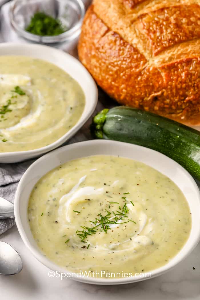 Zucchini Soup is creamy and comforting on a late summer or fall day! This soup is perfect for a quick weeknight meal or lunch on a busy weekend! #spendwithpennies #zucchinisoup #recipe #stovetop #homemade #creamy Zucchini Soup in white bowls with zucchini and bread on the side