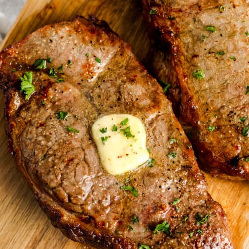 cooked air fryer steaks on a wood board with butter