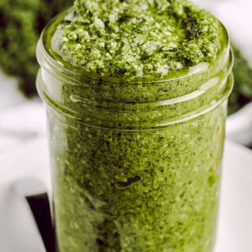 close up of Kale Pesto in a mason jar with a spoon and kale in the background