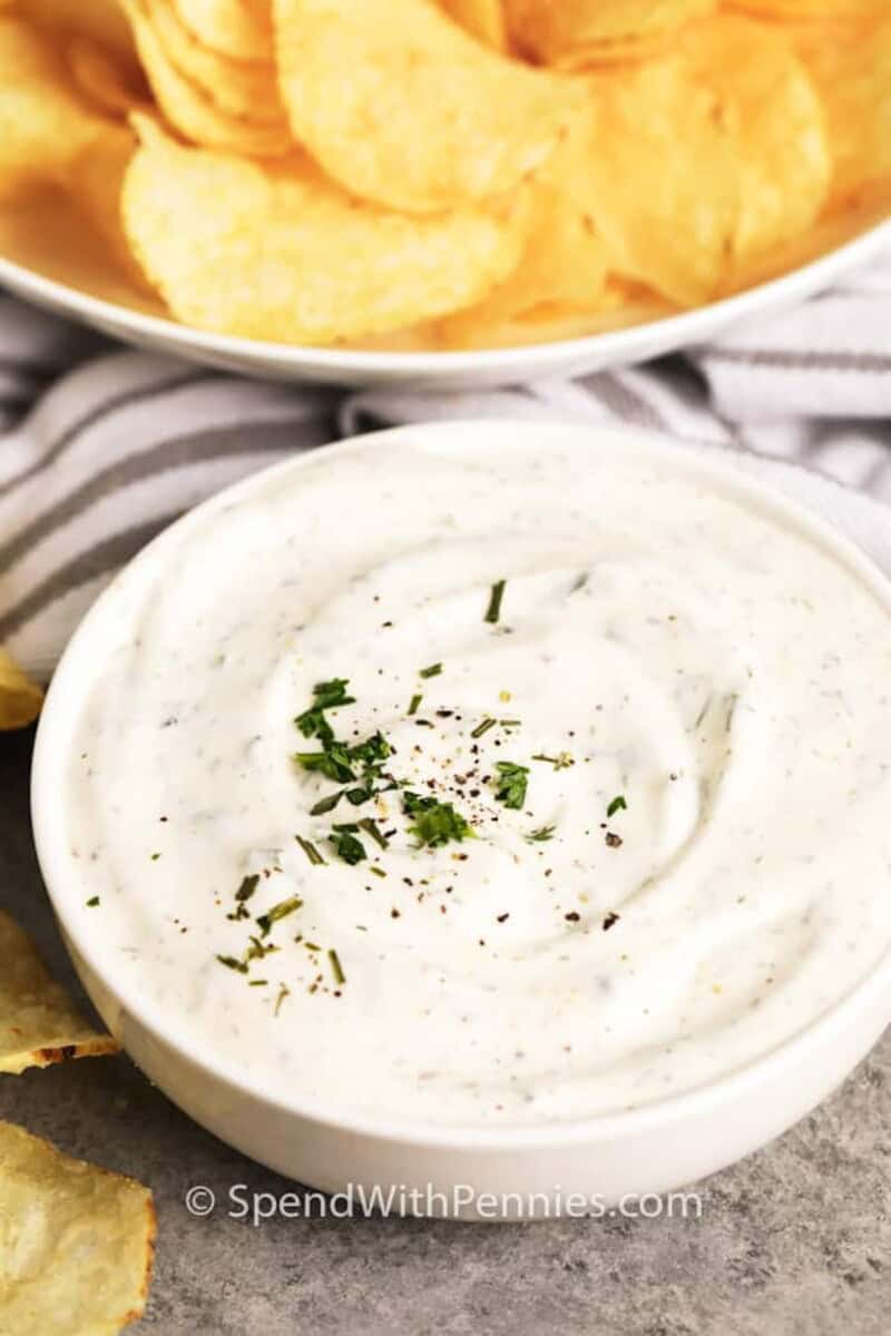 A bowl of sour cream dip with chips in the background.