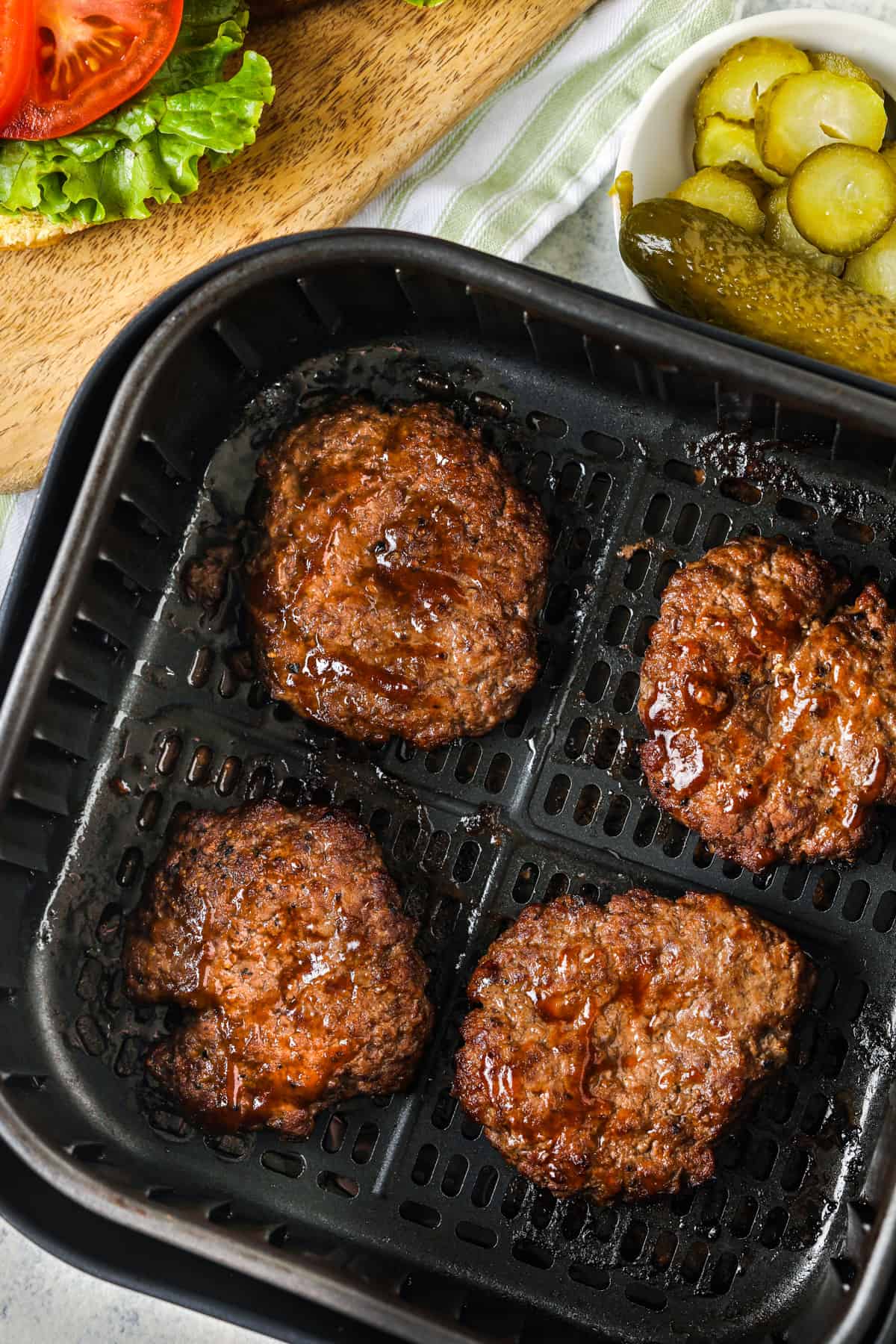 Air Fryer Hamburgeriai oro gruzdintuvėje po kepimo su marinuotais agurkais ir daržovėmis gale