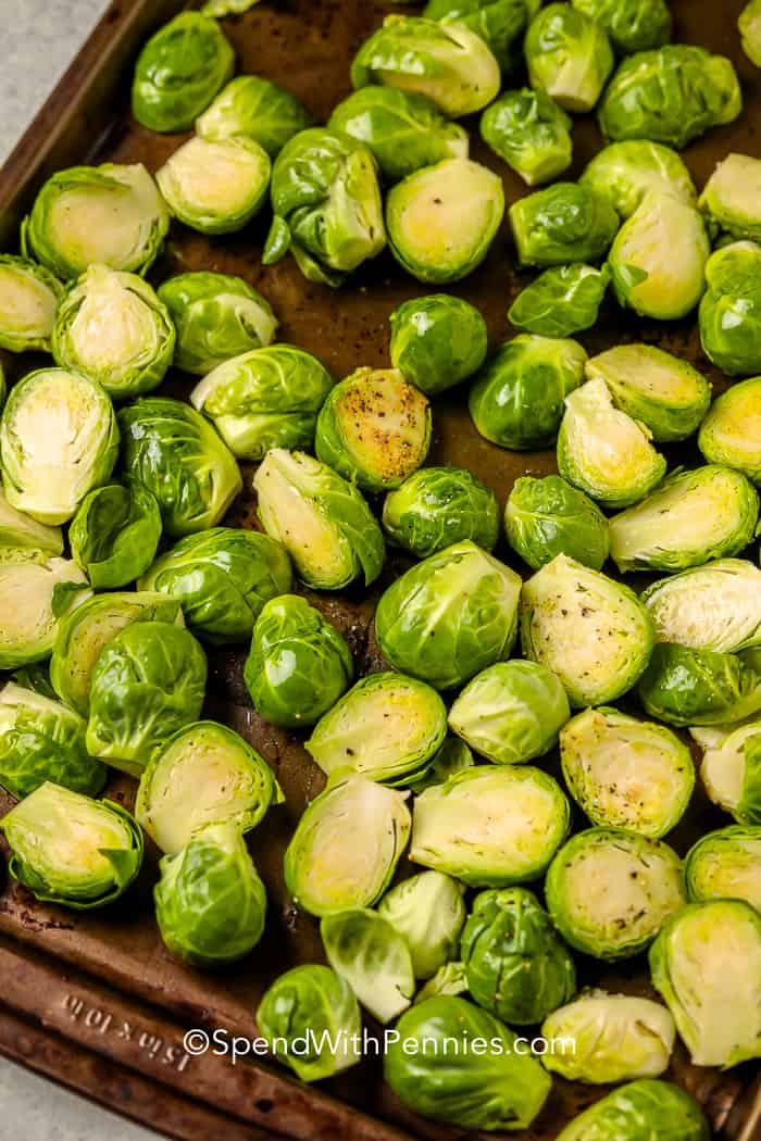 Uncooked, halved brussel sprouts, oiled and seasoned with pepper in a baking tray 